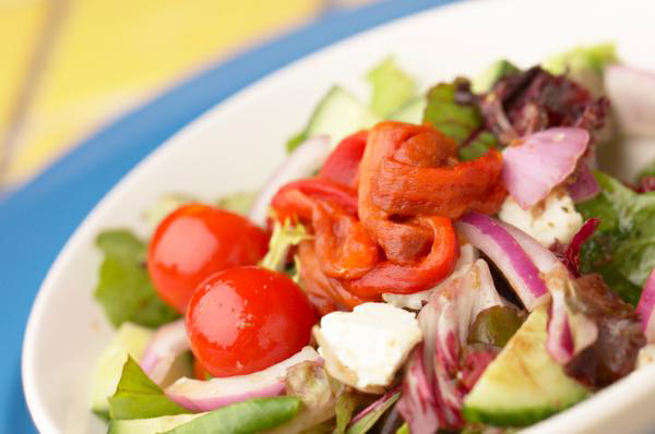 bowl of mixed greens topped with cherry tomatoes, roasted red peppers, red onion, feta, and cucumber