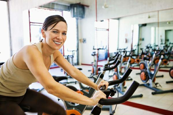 woman smiling while riding a stationary bike in a gym for moderate-intensity aerobic exercise